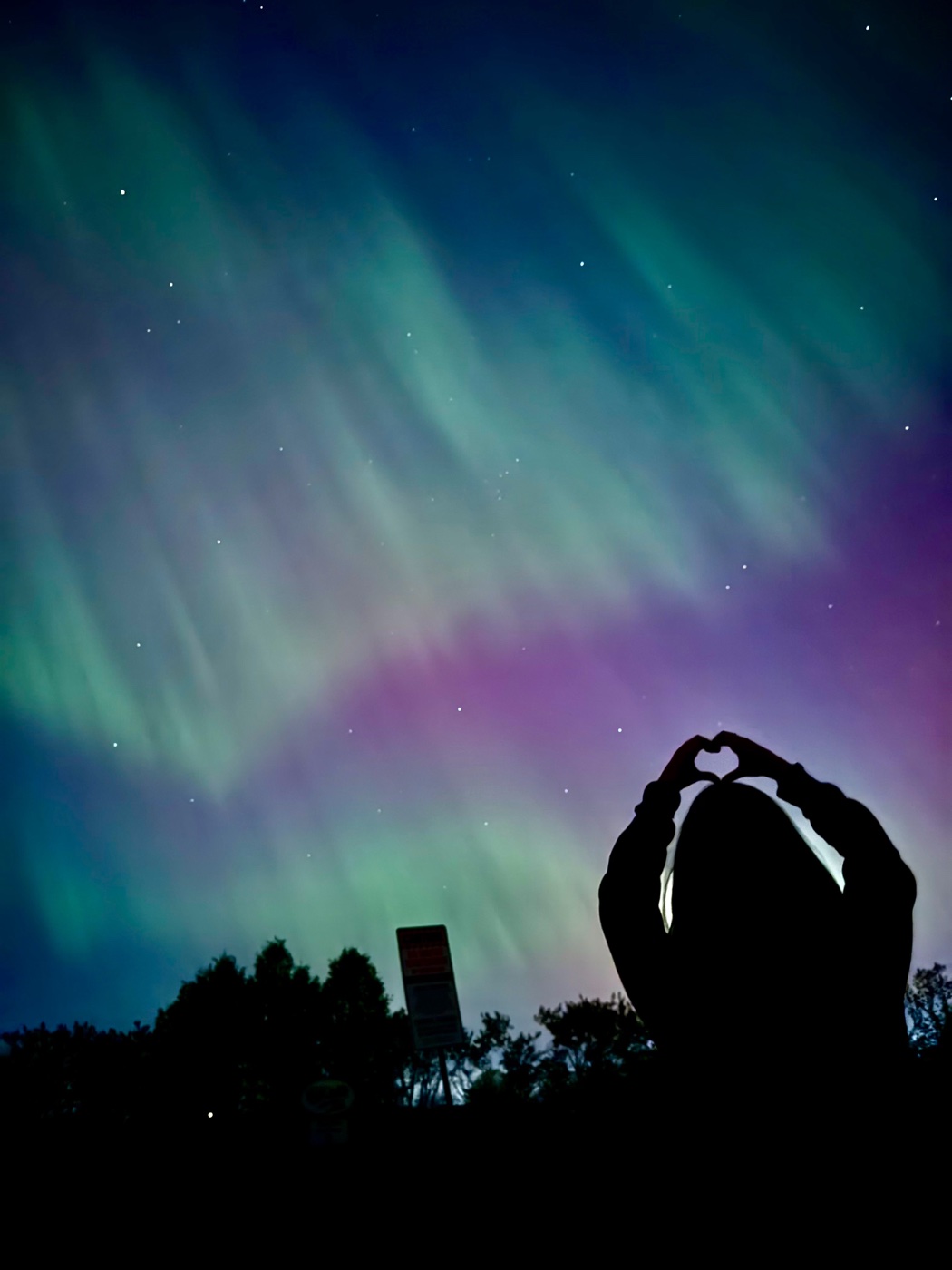 A silhouette making a heart beneath the northern lights
