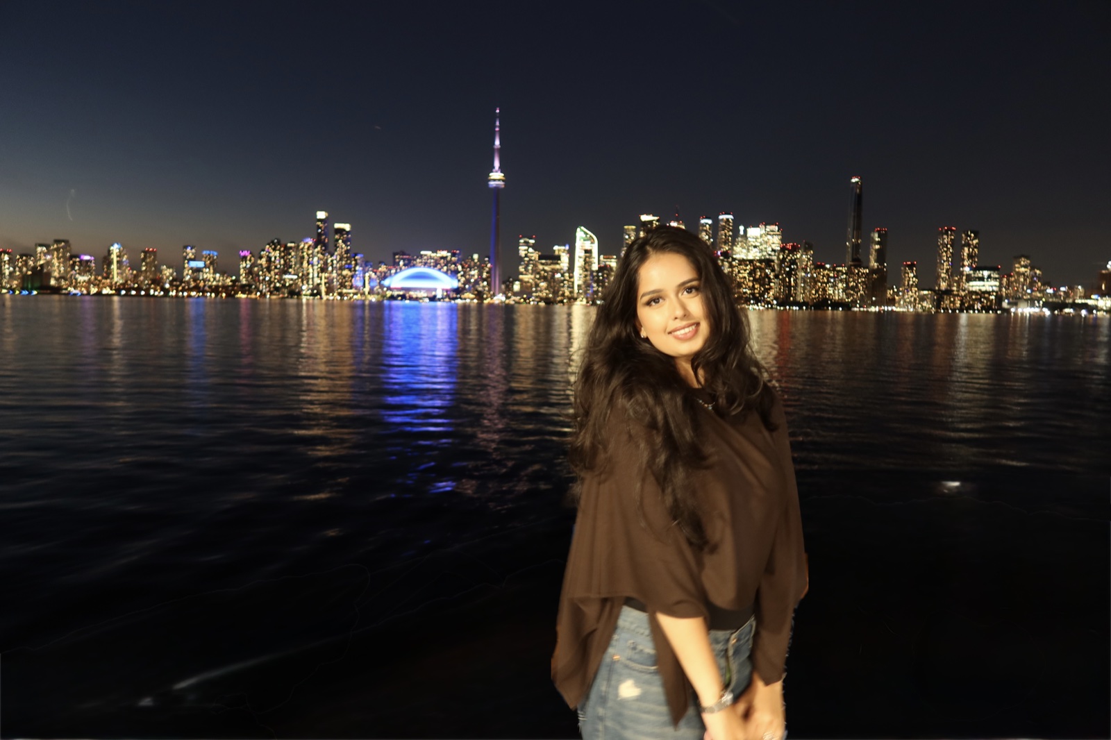 Sarah beside the water with the Toronto skyline at night